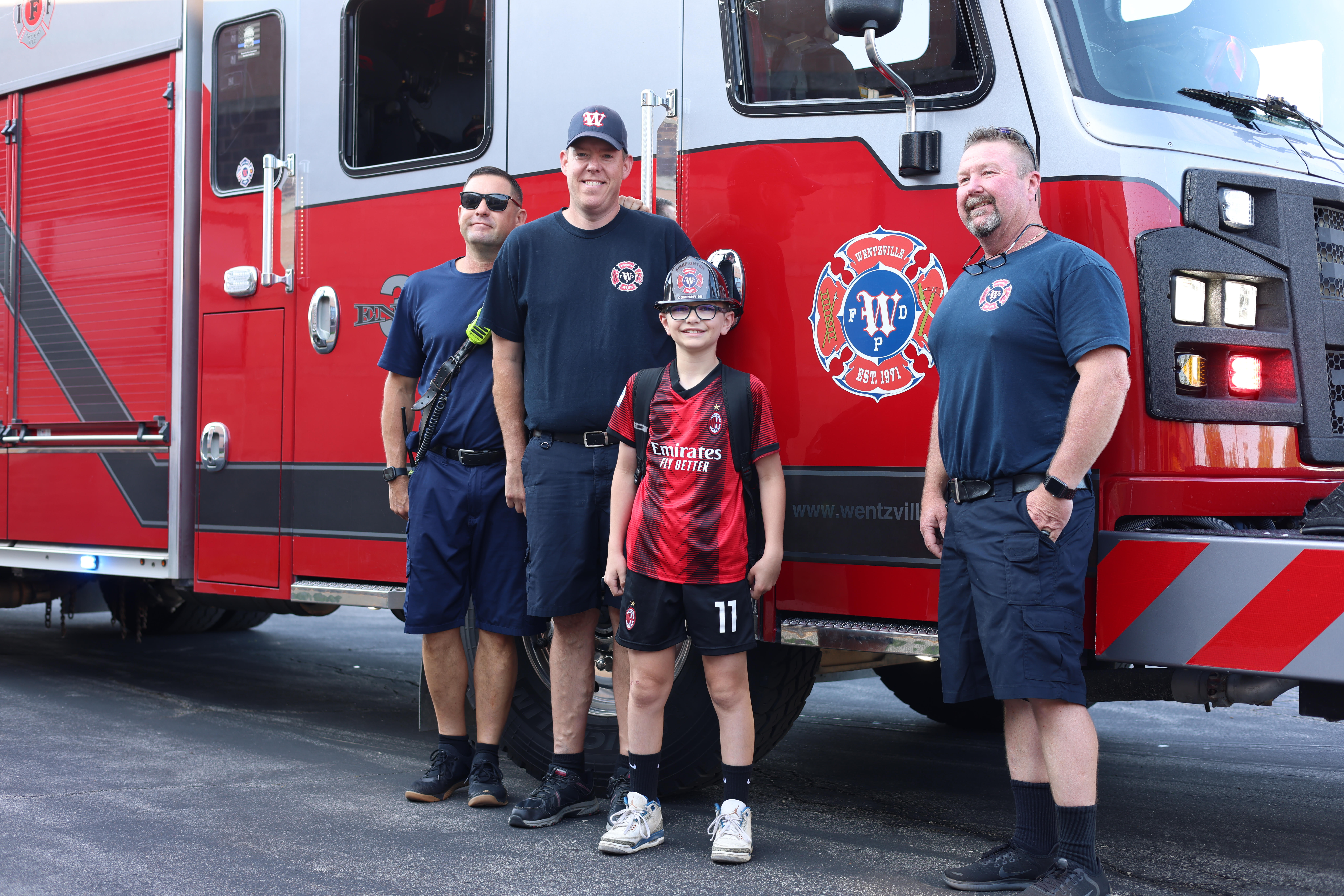 A group of men and a boy posing proudly in front of a fire truck.